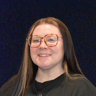 Lead Patient Coordinator Emily Smiling In Front Of Dark Blue Background